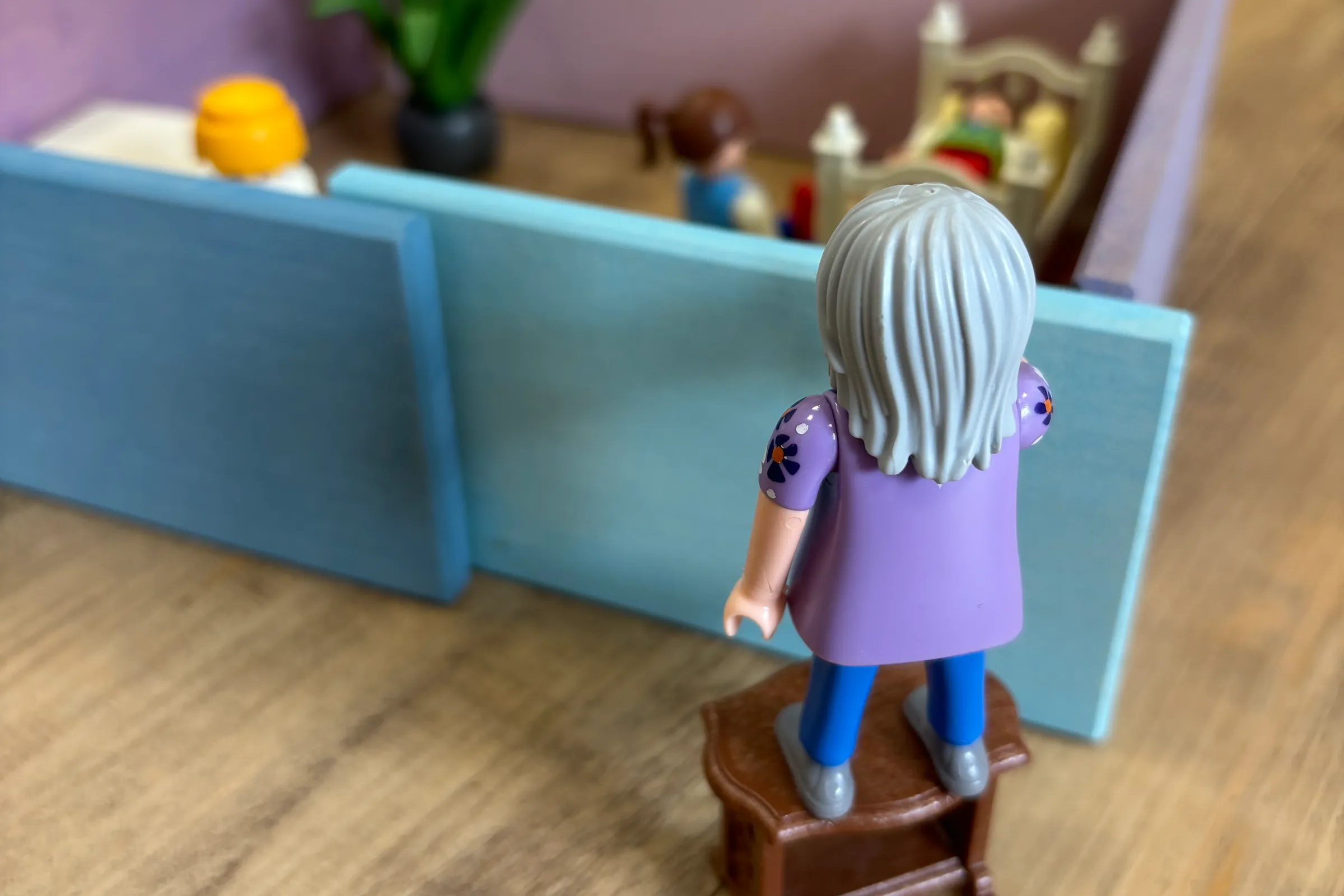 Een speelgoedfiguur kijkt over de wand van een poppenkamer