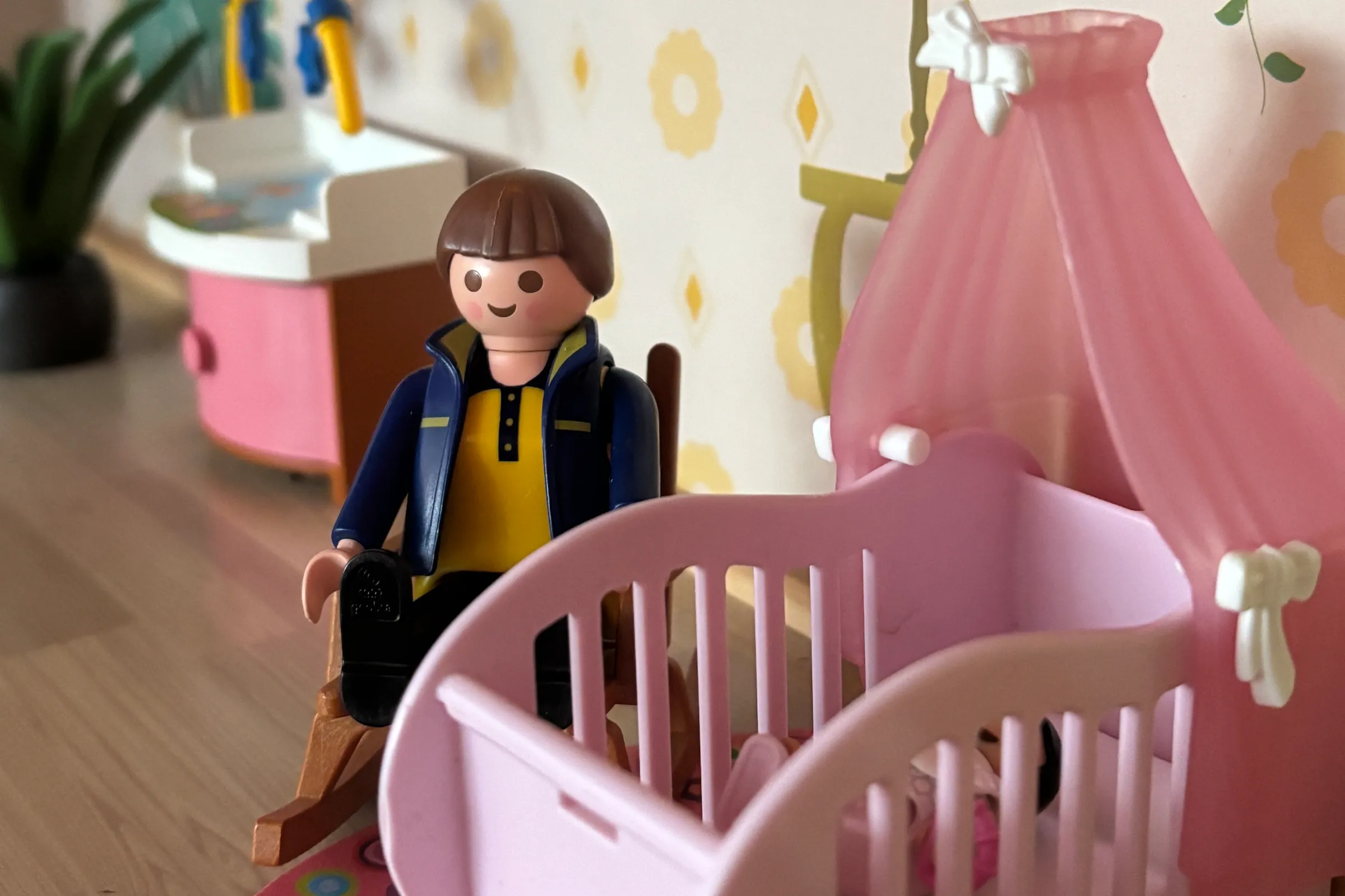 Een speelgoedvader naast een roze wiegje in een poppenhuis
