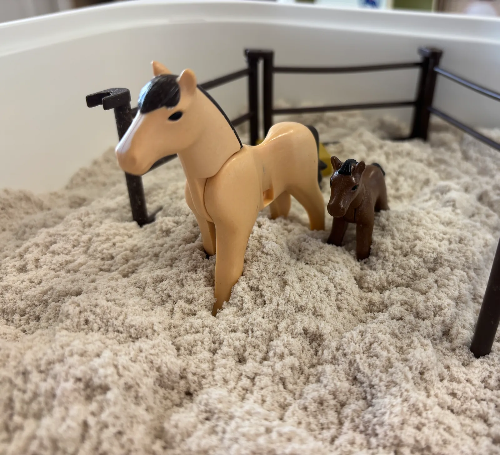 Twee speelgoedpaarden in een zandbak met een hekje